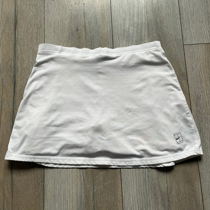 Nike Court Flex Pure Tennis Skirt is a kids’ tennis skort with integrated inner shorts for coverage and support. The skirt is white with a black Nike Swoosh at the lower hem and a Nike Court logo on the opposite side. The front features cut-out sections on both sides for added comfort and mobility.
