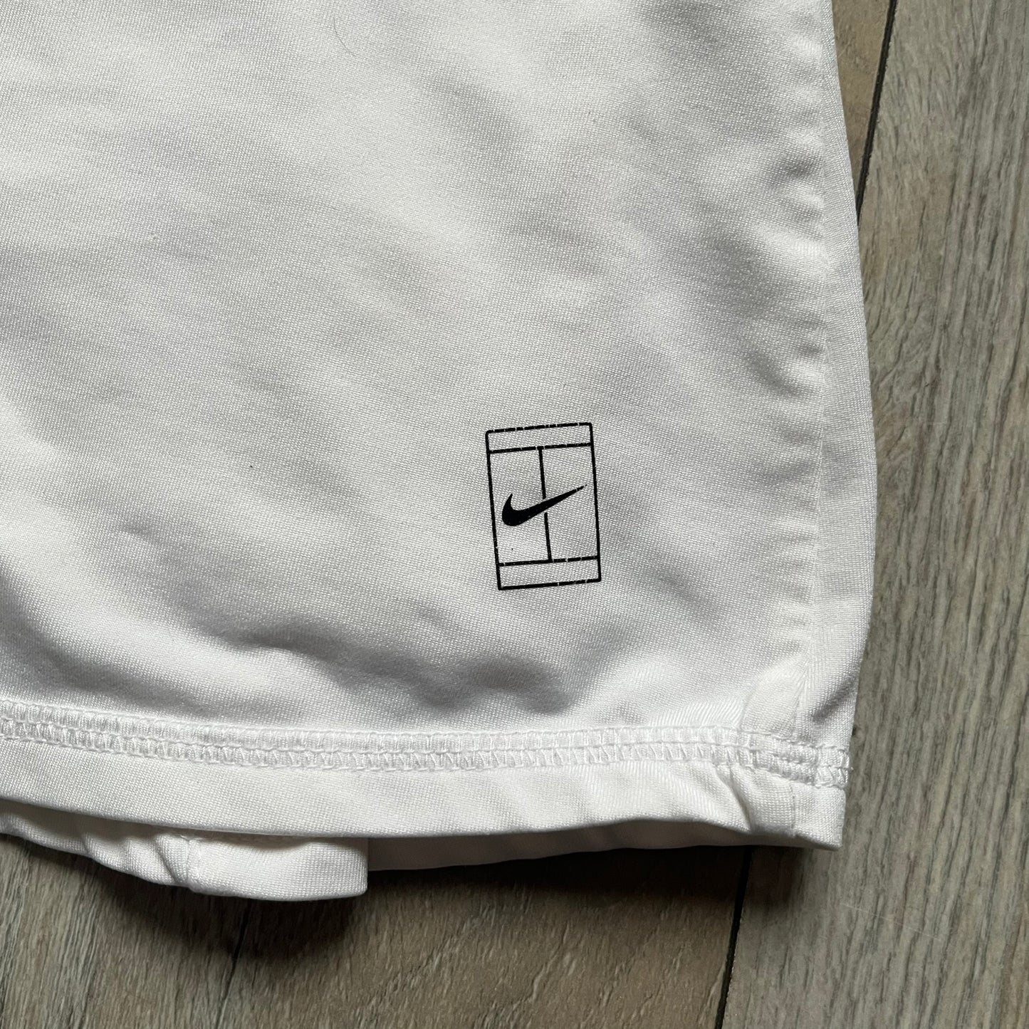 Nike Court Flex Pure Tennis Skirt is a kids’ tennis skort with integrated inner shorts for coverage and support. The skirt is white with a black Nike Swoosh at the lower hem and a Nike Court logo on the opposite side. The front features cut-out sections on both sides for added comfort and mobility.