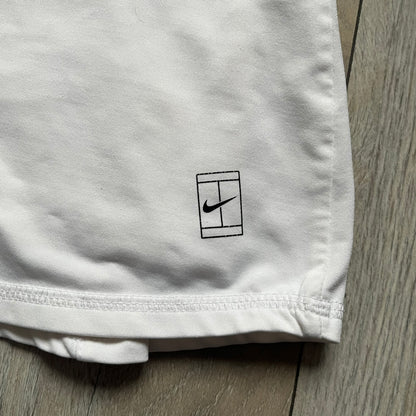 Nike Court Flex Pure Tennis Skirt is a kids’ tennis skort with integrated inner shorts for coverage and support. The skirt is white with a black Nike Swoosh at the lower hem and a Nike Court logo on the opposite side. The front features cut-out sections on both sides for added comfort and mobility.