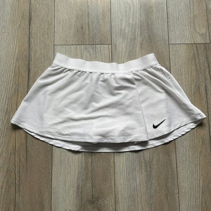 Nike Court Victory Tennis Skirt is a kids’ tennis skort with built-in inner shorts for coverage. The skirt features a textured fabric with fine linear detailing, while the waistband remains smooth, and a black Nike Swoosh is placed at the lower hem. The design includes a pleated section.