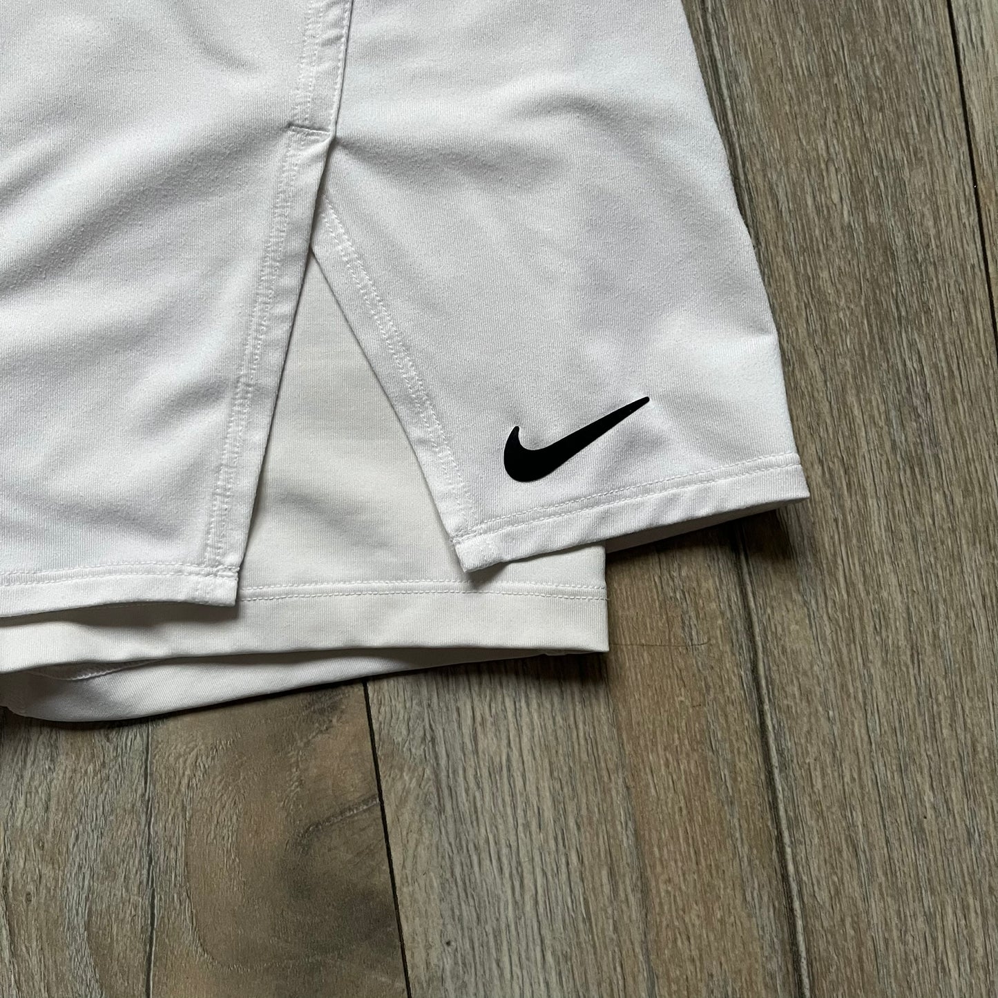 Nike Court Victory W Tennis Skirt is a women’s tennis skort with built-in inner shorts for coverage. The skirt is white with a Nike Swoosh at the lower hem and features a triangular cutout detail next to the logo for added mobility.