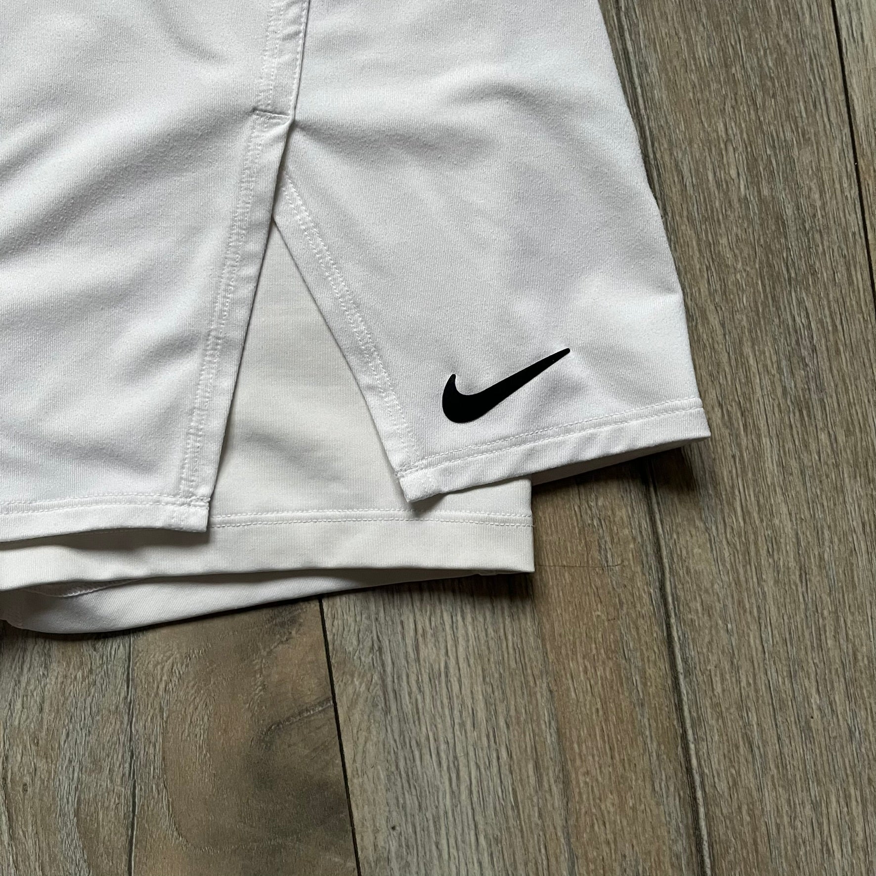 Nike Court Victory W Tennis Skirt is a women’s tennis skort with built-in inner shorts for coverage. The skirt is white with a Nike Swoosh at the lower hem and features a triangular cutout detail next to the logo for added mobility.