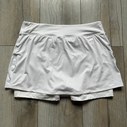 Nike Court Victory W Tennis Skirt is a women’s tennis skort with built-in inner shorts for coverage. The skirt is white with a Nike Swoosh at the lower hem and features a triangular cutout detail next to the logo for added mobility.