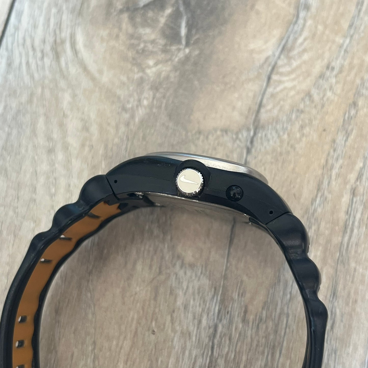 Nike Cross Training VG72-5000 Analog Watch is a 2000s model featuring a black strap, silver-tone stainless steel case, and black dial. The oval-shaped case has a flattened top with an orange Nike Swoosh positioned above the dial. It uses a three-hand analog display and includes an additional button above the crown to operate the backlight.