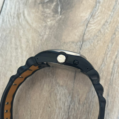 Nike Cross Training VG72-5000 Analog Watch is a 2000s model featuring a black strap, silver-tone stainless steel case, and black dial. The oval-shaped case has a flattened top with an orange Nike Swoosh positioned above the dial. It uses a three-hand analog display and includes an additional button above the crown to operate the backlight.