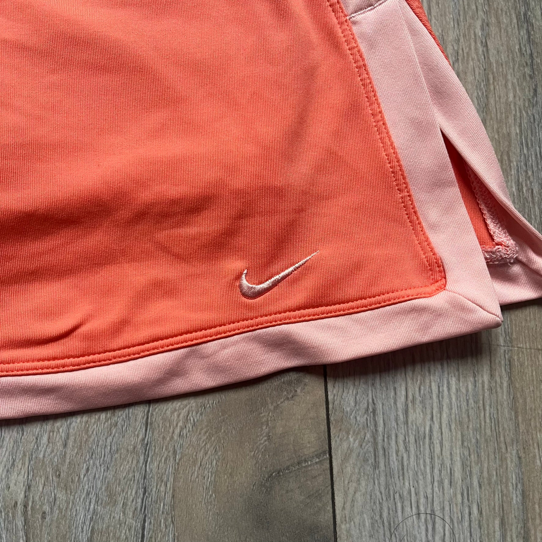 Nike Dri-FIT Orange Tennis Skirt is a women’s tennis skort with built-in shorts for coverage and support. The skirt is finished in orange with lighter side panels and embroidered Nike Swoosh at the lower hem. A small Nike Court logo on the side highlights its connection to Nike’s performance tennis line.