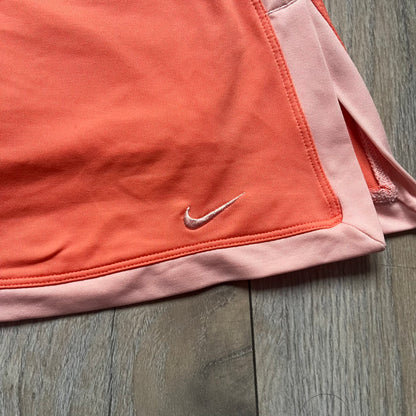 Nike Dri-FIT Orange Tennis Skirt is a women’s tennis skort with built-in shorts for coverage and support. The skirt is finished in orange with lighter side panels and embroidered Nike Swoosh at the lower hem. A small Nike Court logo on the side highlights its connection to Nike’s performance tennis line.