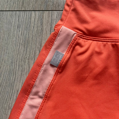Nike Dri-FIT Orange Tennis Skirt is a women’s tennis skort with built-in shorts for coverage and support. The skirt is finished in orange with lighter side panels and embroidered Nike Swoosh at the lower hem. A small Nike Court logo on the side highlights its connection to Nike’s performance tennis line.