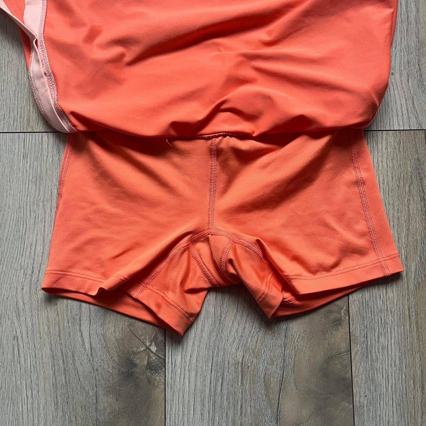Nike Dri-FIT Orange Tennis Skirt is a women’s tennis skort with built-in shorts for coverage and support. The skirt is finished in orange with lighter side panels and embroidered Nike Swoosh at the lower hem. A small Nike Court logo on the side highlights its connection to Nike’s performance tennis line.
