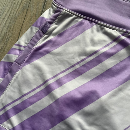 Nike Dri-FIT Striped Lavender Tennis Skirt is a women’s tennis skort with integrated inner shorts for coverage and support. The skirt features diagonal white and lavender stripes on the front and back, a small Nike Court logo on the side, and an embroidered lavender Swoosh at the lower front. The lavender waistband and side cutouts provide comfort and mobility during play.