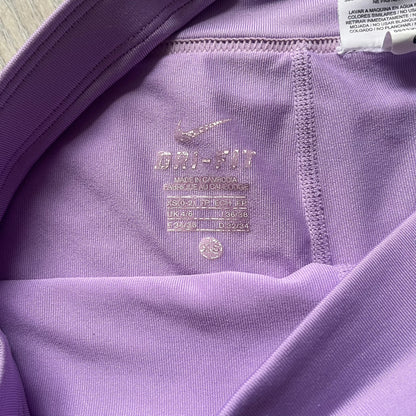 Nike Dri-FIT Striped Lavender Tennis Skirt is a women’s tennis skort with integrated inner shorts for coverage and support. The skirt features diagonal white and lavender stripes on the front and back, a small Nike Court logo on the side, and an embroidered lavender Swoosh at the lower front. The lavender waistband and side cutouts provide comfort and mobility during play.