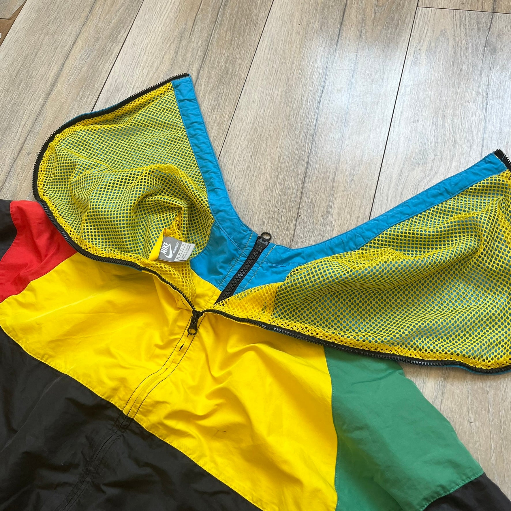 Nike Ethiopia Olympics 2008 Split Windbreaker is a performance jacket designed by Jarrett Reynolds for the Olympic collection. The jacket features a black lower section, yellow upper body, blue hood, green shoulder and red opposite shoulder. The chest is finished with an embroidered Nike logo and Ethiopia emblem. The jacket features a unique split construction that allows it to be unzipped along both sides and connected with other compatible jackets. Hidden inside, a small Ethiopia flags accent completes th