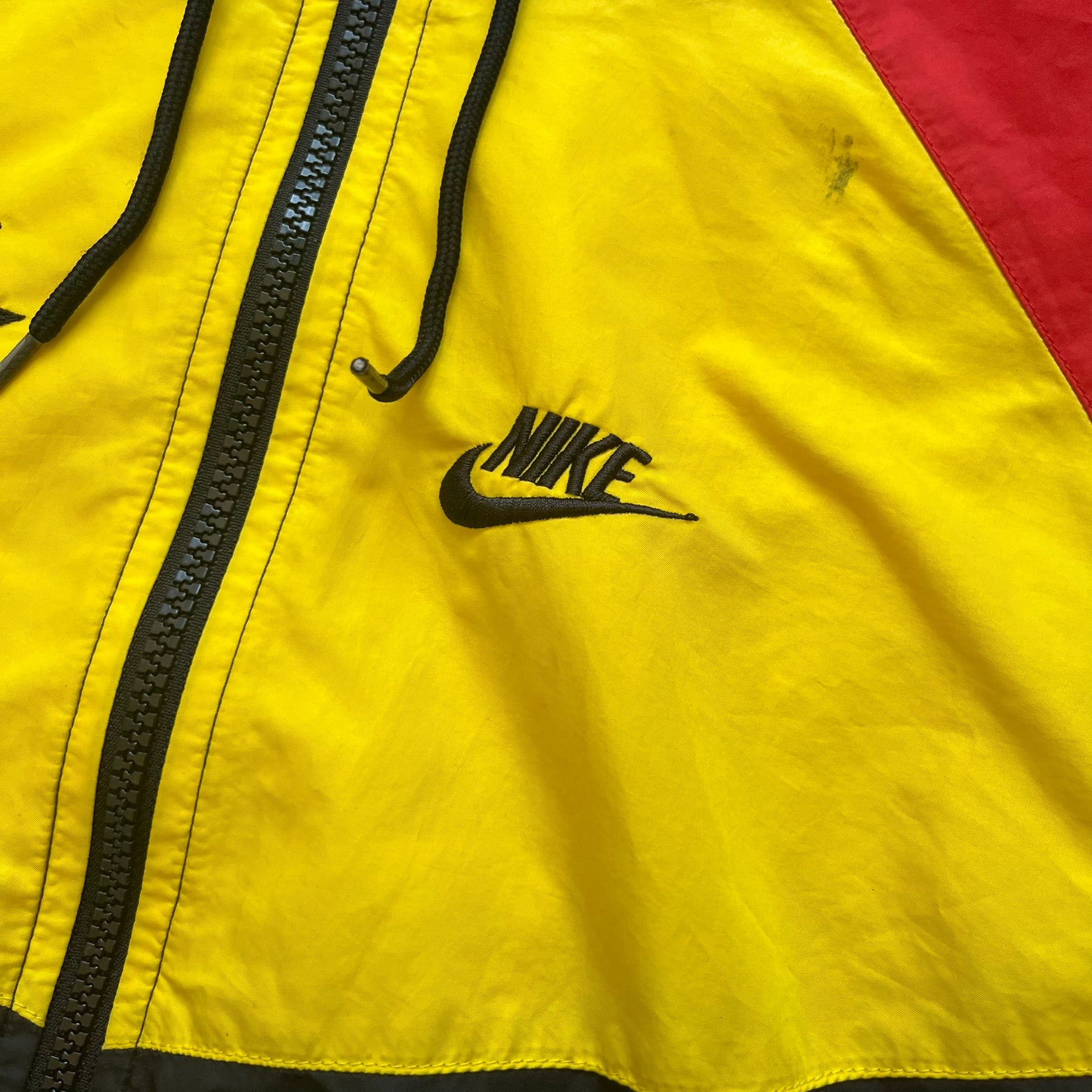 Nike Ethiopia Olympics 2008 Split Windbreaker is a performance jacket designed by Jarrett Reynolds for the Olympic collection. The jacket features a black lower section, yellow upper body, blue hood, green shoulder and red opposite shoulder. The chest is finished with an embroidered Nike logo and Ethiopia emblem. The jacket features a unique split construction that allows it to be unzipped along both sides and connected with other compatible jackets. Hidden inside, a small Ethiopia flags accent completes th