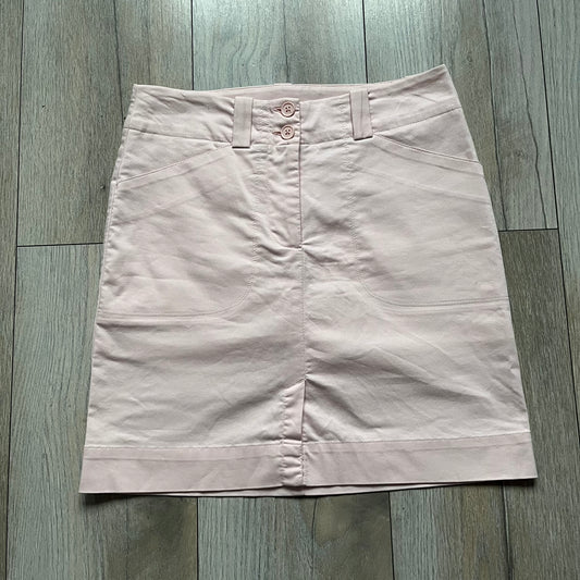 Nike Fit-Dry Light Pink Golf Skirt is a women’s golf skort with integrated inner shorts. The light pink skirt features belt loops at the waistband, front and back pockets, side cutouts for flexibility, and a button closure. A small embroidered Nike logo is placed at the back, maintaining a minimal design.