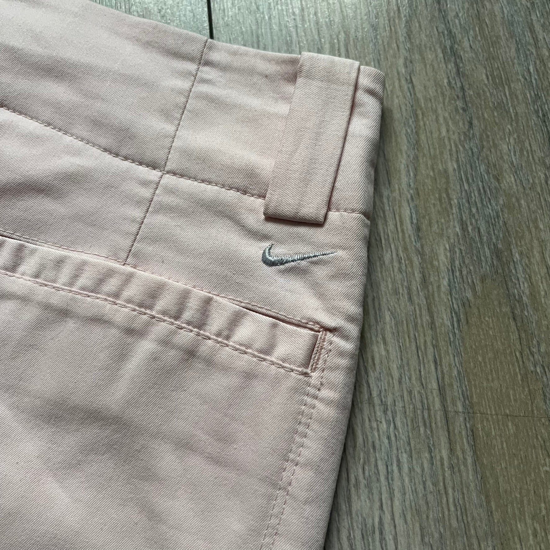 Nike Fit-Dry Light Pink Golf Skirt is a women’s golf skort with integrated inner shorts. The light pink skirt features belt loops at the waistband, front and back pockets, side cutouts for flexibility, and a button closure. A small embroidered Nike logo is placed at the back, maintaining a minimal design.