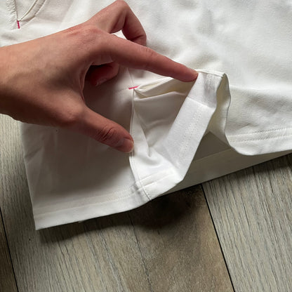 Nike Fit Dry White/Pink Golf Skirt is a women’s golf skort with built-in inner shorts. The white skirt features belt loops at the waistband, front pockets, a small back pocket, and side cutouts on both sides for flexibility. Below the left front pocket there is a small pink floral-style detail along with a Nike Golf patch.