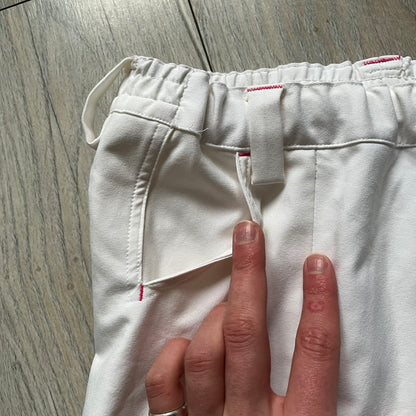 Nike Fit Dry White/Pink Golf Skirt is a women’s golf skort with built-in inner shorts. The white skirt features belt loops at the waistband, front pockets, a small back pocket, and side cutouts on both sides for flexibility. Below the left front pocket there is a small pink floral-style detail along with a Nike Golf patch.