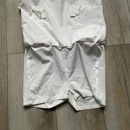 Nike Fit Dry White/Pink Golf Skirt is a women’s golf skort with built-in inner shorts. The white skirt features belt loops at the waistband, front pockets, a small back pocket, and side cutouts on both sides for flexibility. Below the left front pocket there is a small pink floral-style detail along with a Nike Golf patch.