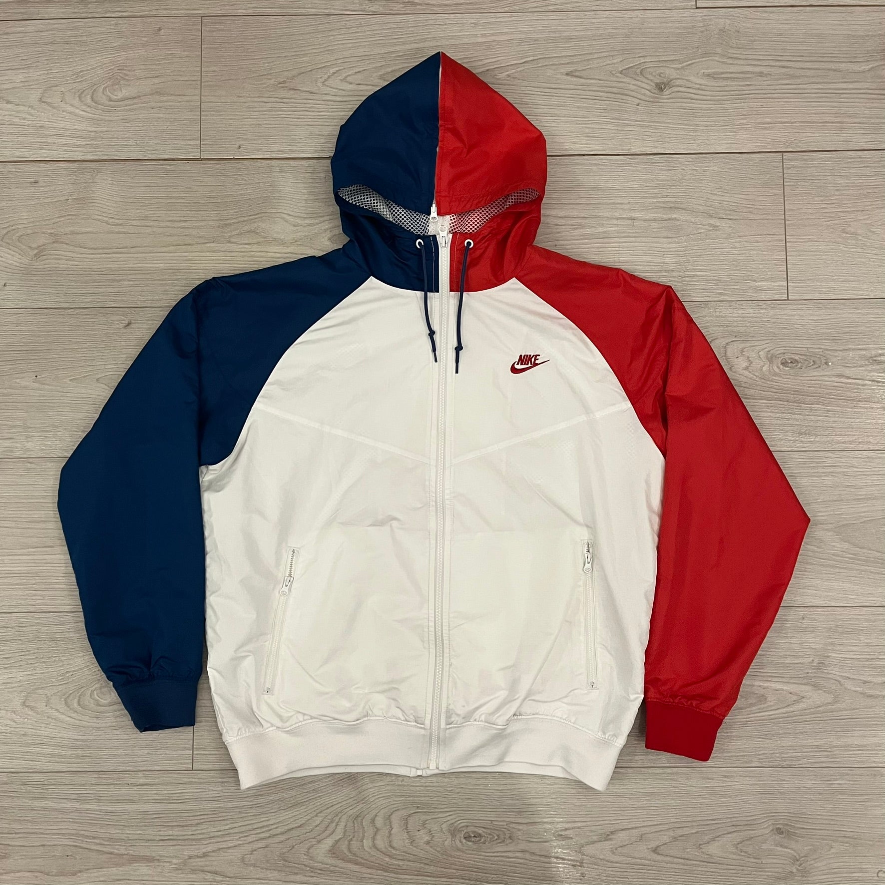 The Nike France Olympics 2008 Split Windbreaker made in a white, red, and navy color block representing France, it includes a red embroidered Nike logo and hidden French flags inside both pockets. It features a modular design by Jarrett Reynolds, allowing the jacket to split on both sides via dual zippers.