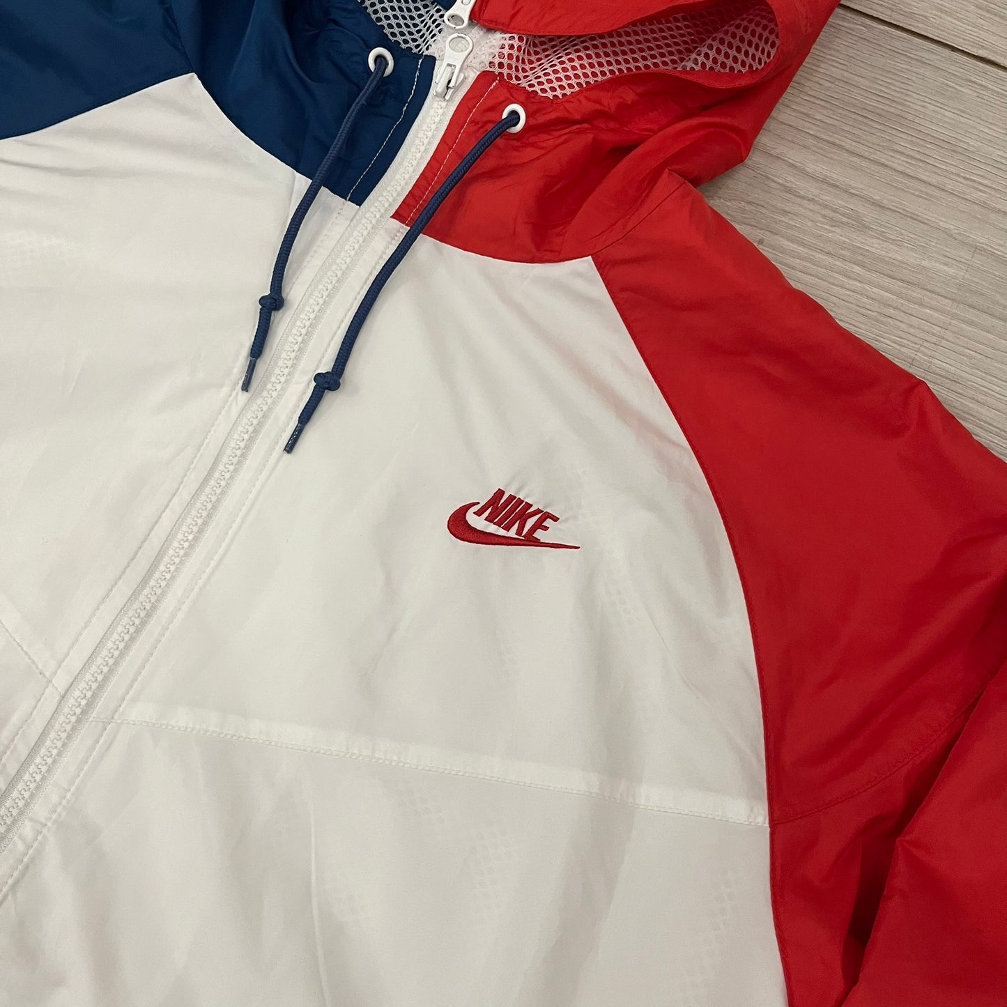 The Nike France Olympics 2008 Split Windbreaker made in a white, red, and navy color block representing France, it includes a red embroidered Nike logo and hidden French flags inside both pockets. It features a modular design by Jarrett Reynolds, allowing the jacket to split on both sides via dual zippers.