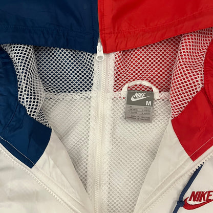 The Nike France Olympics 2008 Split Windbreaker made in a white, red, and navy color block representing France, it includes a red embroidered Nike logo and hidden French flags inside both pockets. It features a modular design by Jarrett Reynolds, allowing the jacket to split on both sides via dual zippers.