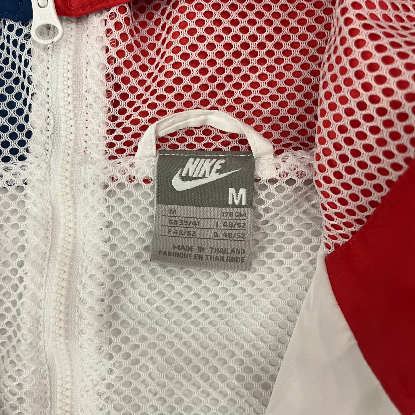 The Nike France Olympics 2008 Split Windbreaker made in a white, red, and navy color block representing France, it includes a red embroidered Nike logo and hidden French flags inside both pockets. It features a modular design by Jarrett Reynolds, allowing the jacket to split on both sides via dual zippers.