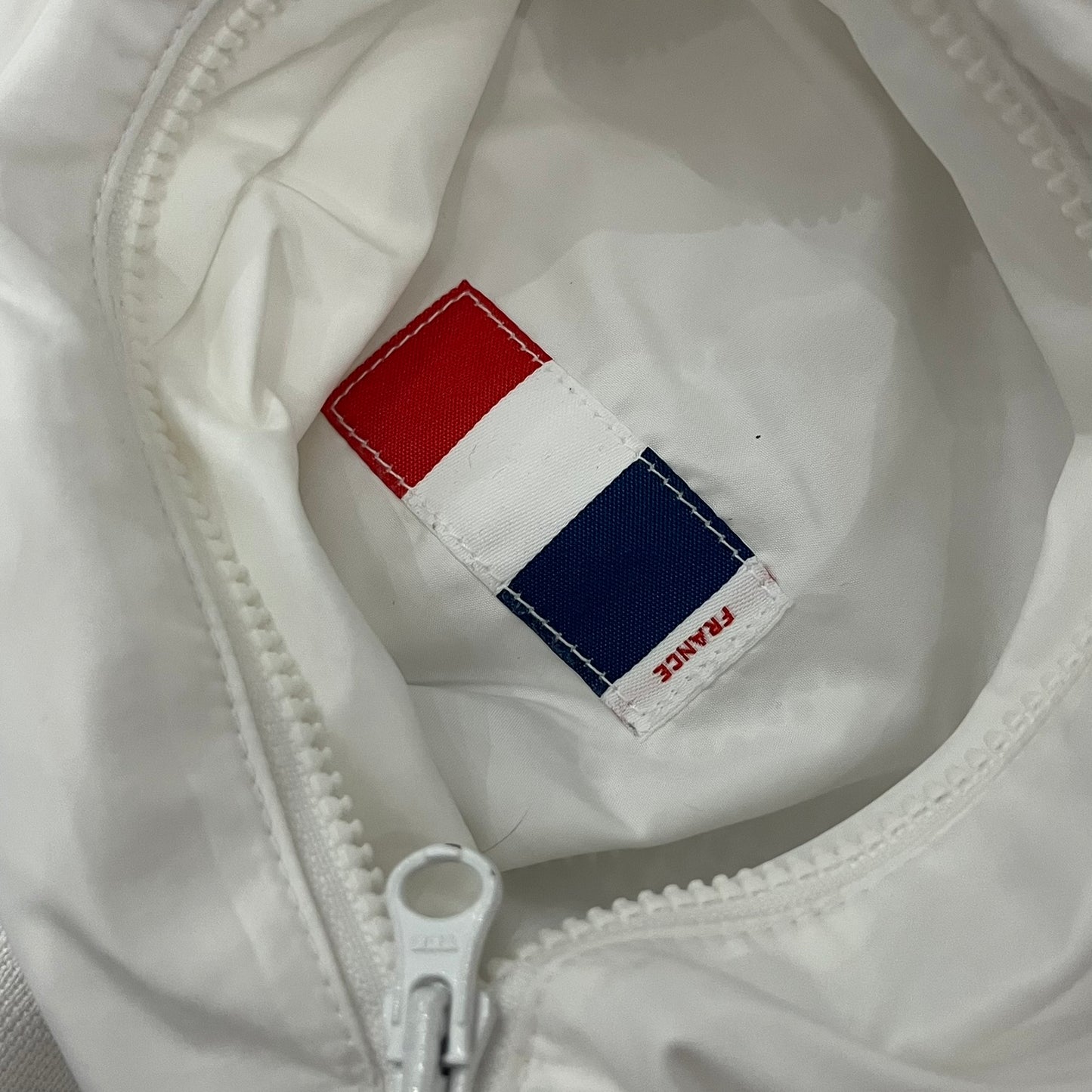 The Nike France Olympics 2008 Split Windbreaker made in a white, red, and navy color block representing France, it includes a red embroidered Nike logo and hidden French flags inside both pockets. It features a modular design by Jarrett Reynolds, allowing the jacket to split on both sides via dual zippers.