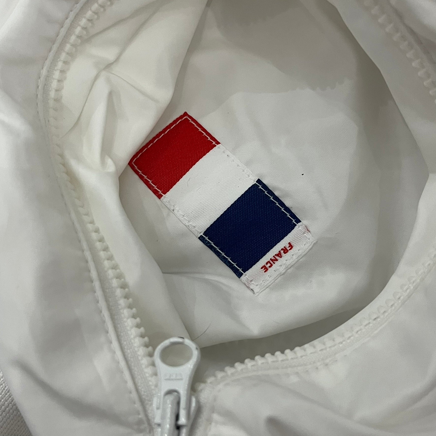 The Nike France Olympics 2008 Split Windbreaker made in a white, red, and navy color block representing France, it includes a red embroidered Nike logo and hidden French flags inside both pockets. It features a modular design by Jarrett Reynolds, allowing the jacket to split on both sides via dual zippers.