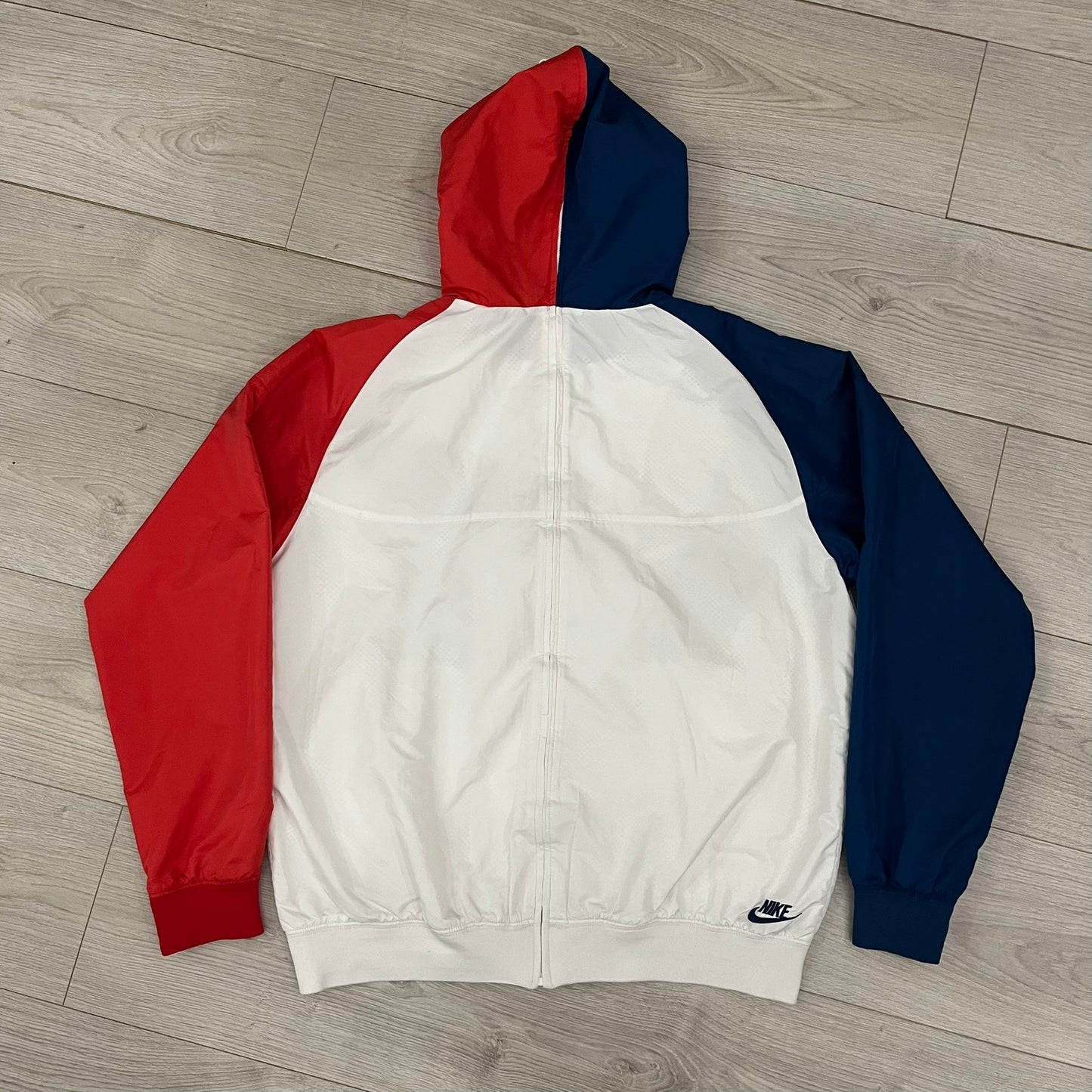 The Nike France Olympics 2008 Split Windbreaker made in a white, red, and navy color block representing France, it includes a red embroidered Nike logo and hidden French flags inside both pockets. It features a modular design by Jarrett Reynolds, allowing the jacket to split on both sides via dual zippers.
