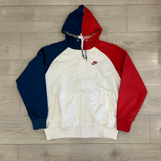 The Nike France Olympics 2008 Split Windbreaker made in a white, red, and navy color block representing France, it includes a red embroidered Nike logo and hidden French flags inside both pockets. It features a modular design by Jarrett Reynolds, allowing the jacket to split on both sides via dual zippers.