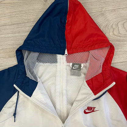 The Nike France Olympics 2008 Split Windbreaker made in a white, red, and navy color block representing France, it includes a red embroidered Nike logo and hidden French flags inside both pockets. It features a modular design by Jarrett Reynolds, allowing the jacket to split on both sides via dual zippers.
