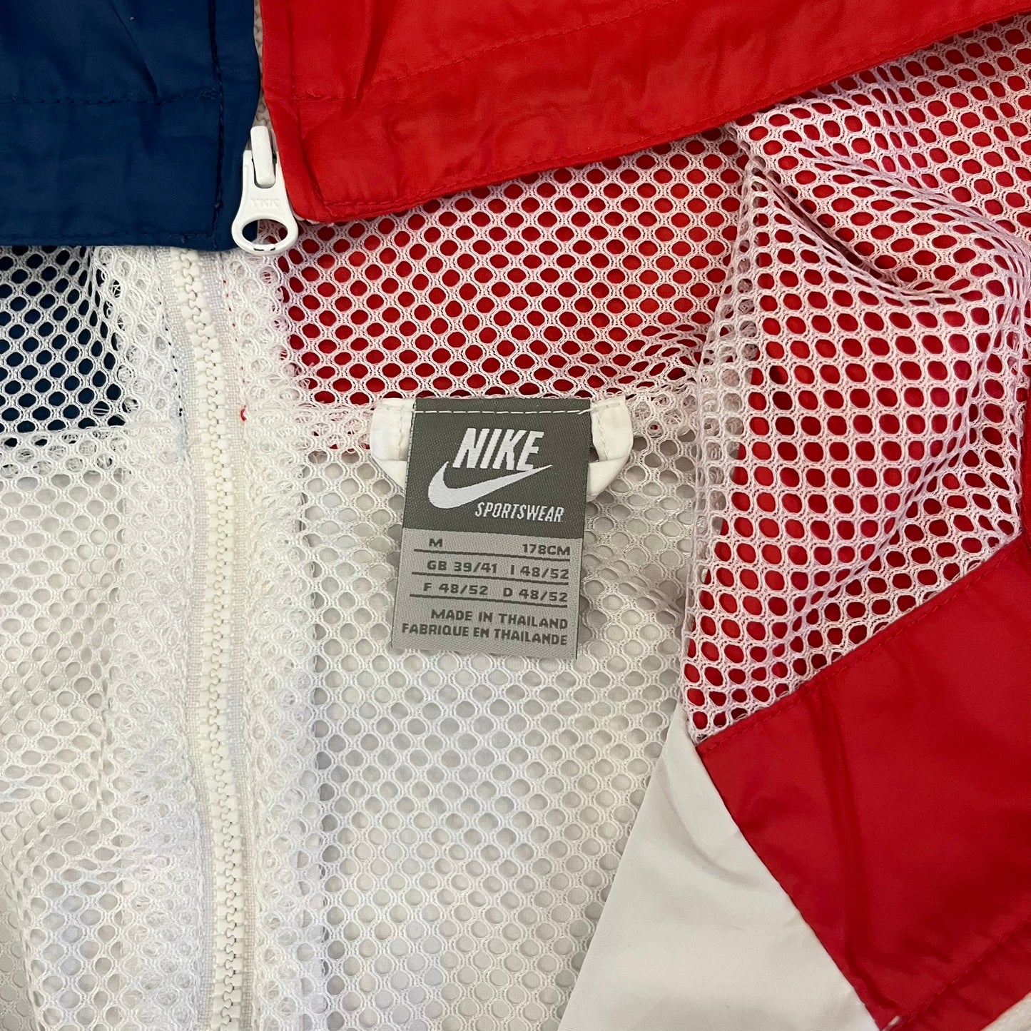 The Nike France Olympics 2008 Split Windbreaker made in a white, red, and navy color block representing France, it includes a red embroidered Nike logo and hidden French flags inside both pockets. It features a modular design by Jarrett Reynolds, allowing the jacket to split on both sides via dual zippers.