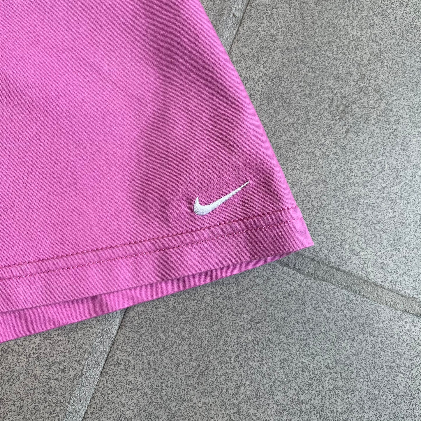 Nike Fuchsia Pleated Skirt features a vibrant fuchsia colorway with a pleated design and a center slit for improved freedom of movement. It is detailed with a small white Nike Swoosh near the hem and a Nike Tennis logo at the waistband. The skirt fastens with a button and zip closure and is finished with contrasting white stitching for a sporty look.