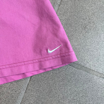 Nike Fuchsia Pleated Skirt features a vibrant fuchsia colorway with a pleated design and a center slit for improved freedom of movement. It is detailed with a small white Nike Swoosh near the hem and a Nike Tennis logo at the waistband. The skirt fastens with a button and zip closure and is finished with contrasting white stitching for a sporty look.