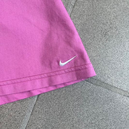 Nike Fuchsia Pleated Skirt features a vibrant fuchsia colorway with a pleated design and a center slit for improved freedom of movement. It is detailed with a small white Nike Swoosh near the hem and a Nike Tennis logo at the waistband. The skirt fastens with a button and zip closure and is finished with contrasting white stitching for a sporty look.