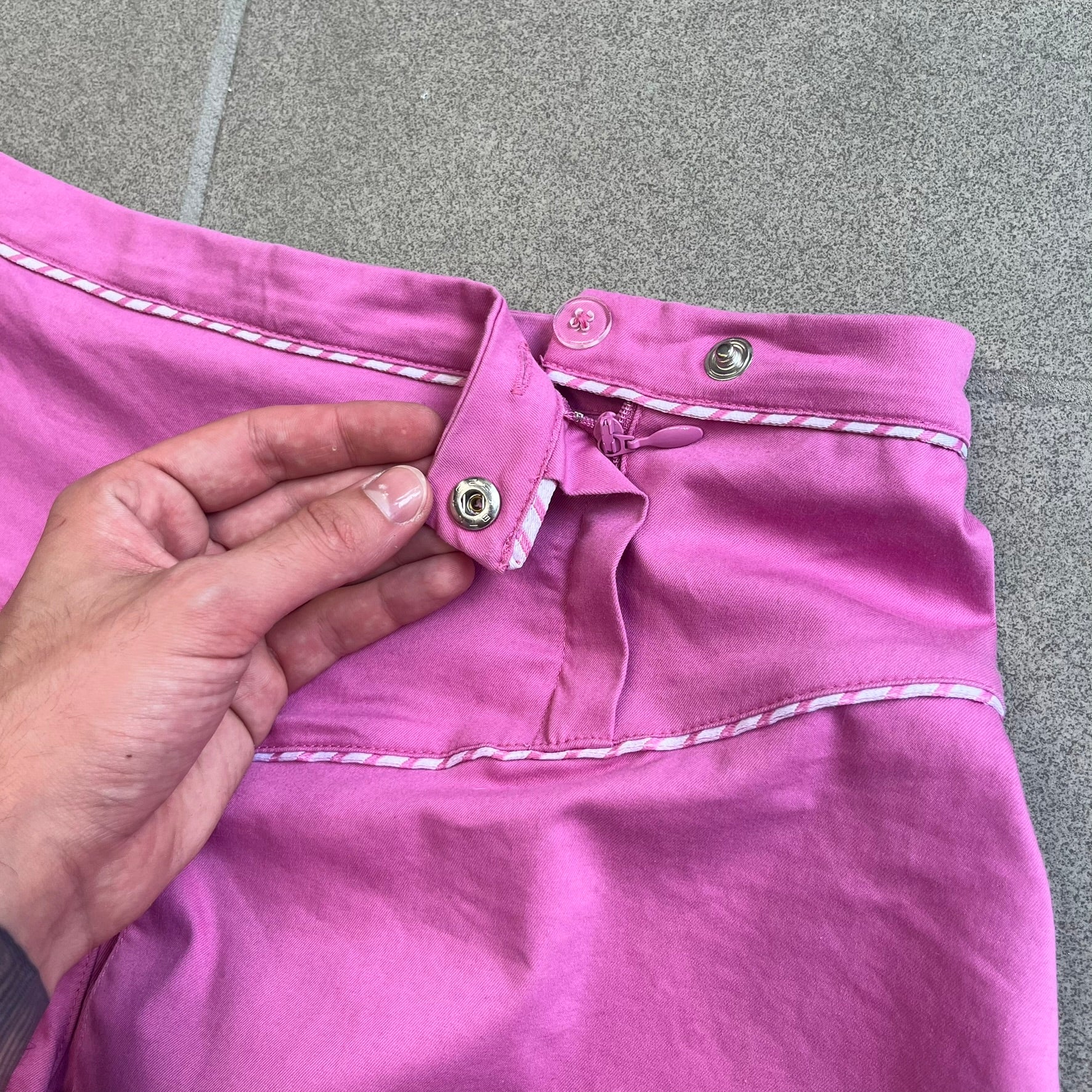 Nike Fuchsia Pleated Skirt features a vibrant fuchsia colorway with a pleated design and a center slit for improved freedom of movement. It is detailed with a small white Nike Swoosh near the hem and a Nike Tennis logo at the waistband. The skirt fastens with a button and zip closure and is finished with contrasting white stitching for a sporty look.