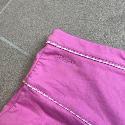 Nike Fuchsia Pleated Skirt features a vibrant fuchsia colorway with a pleated design and a center slit for improved freedom of movement. It is detailed with a small white Nike Swoosh near the hem and a Nike Tennis logo at the waistband. The skirt fastens with a button and zip closure and is finished with contrasting white stitching for a sporty look.