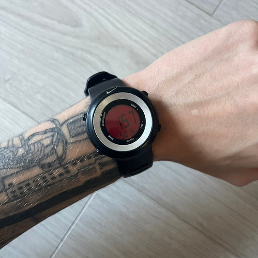 Nike Georg WK0010 digital watch with a bold red dial and black case accented by a silver aluminum bezel. Features include chronograph, alarm, time, and date functions with a 12-hour display and backlight. Water-resistant up to 50m with a durable black silicone strap.