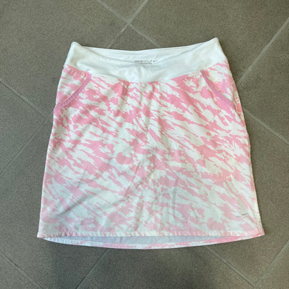 Nike Golf Pink & White Animal Print Skort features a white base with a pink animal-style camouflage pattern that gradually fades toward the lower section. It has built-in white shorts underneath, an embroidered Nike logo at the bottom corner, and pockets on both the front and back.
