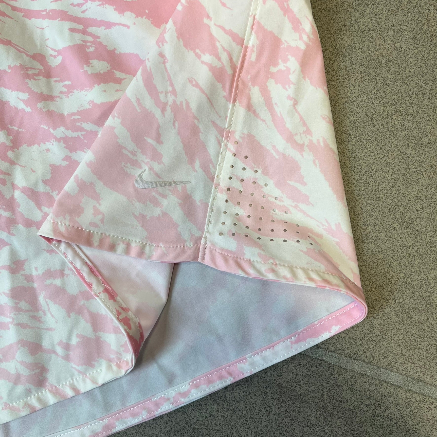 Nike Golf Pink & White Animal Print Skort features a white base with a pink animal-style camouflage pattern that gradually fades toward the lower section. It has built-in white shorts underneath, an embroidered Nike logo at the bottom corner, and pockets on both the front and back.
