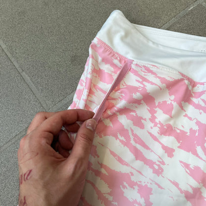 Nike Golf Pink & White Animal Print Skort features a white base with a pink animal-style camouflage pattern that gradually fades toward the lower section. It has built-in white shorts underneath, an embroidered Nike logo at the bottom corner, and pockets on both the front and back.
