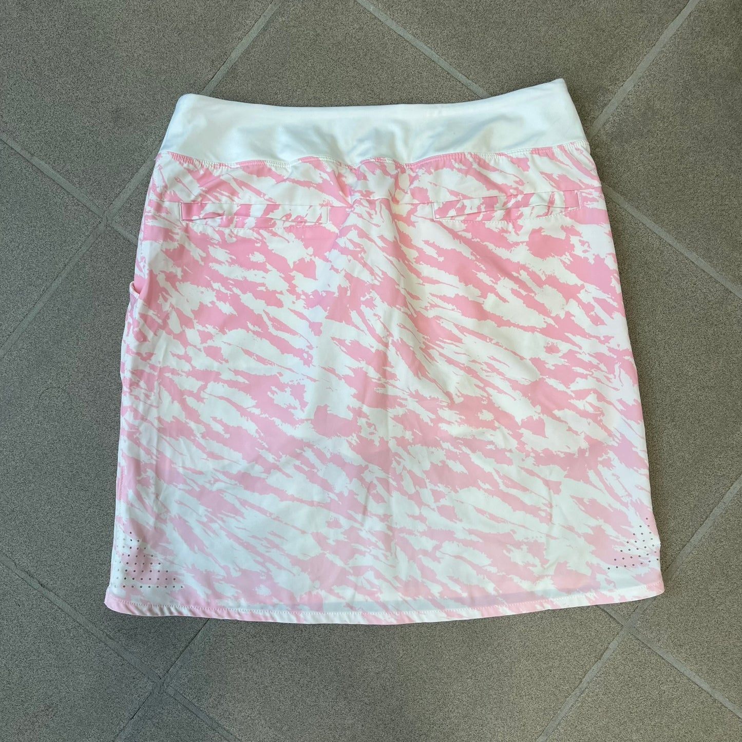 Nike Golf Pink & White Animal Print Skort features a white base with a pink animal-style camouflage pattern that gradually fades toward the lower section. It has built-in white shorts underneath, an embroidered Nike logo at the bottom corner, and pockets on both the front and back.
