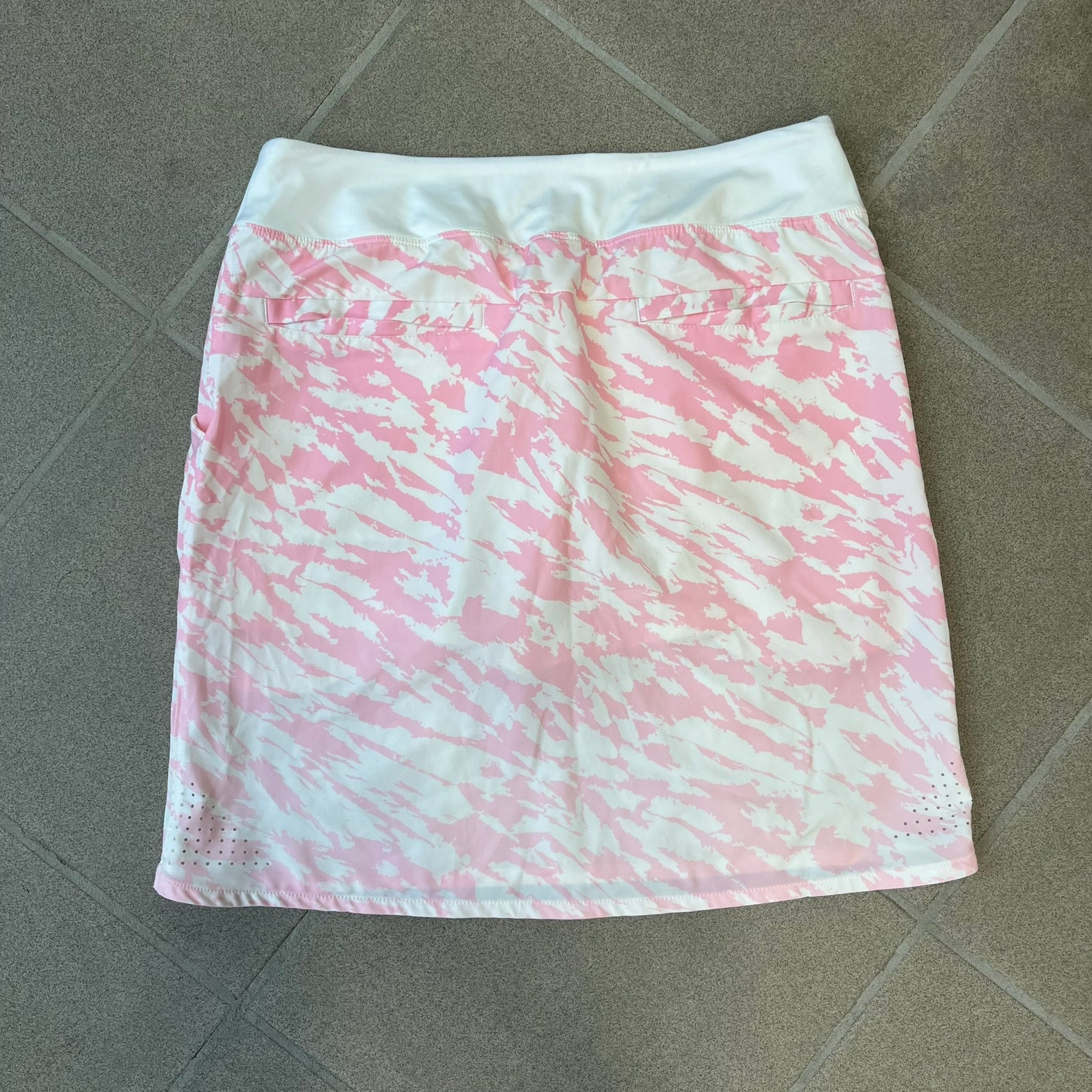 Nike Golf Pink & White Animal Print Skort features a white base with a pink animal-style camouflage pattern that gradually fades toward the lower section. It has built-in white shorts underneath, an embroidered Nike logo at the bottom corner, and pockets on both the front and back.
