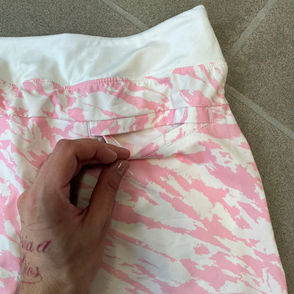 Nike Golf Pink & White Animal Print Skort features a white base with a pink animal-style camouflage pattern that gradually fades toward the lower section. It has built-in white shorts underneath, an embroidered Nike logo at the bottom corner, and pockets on both the front and back.
