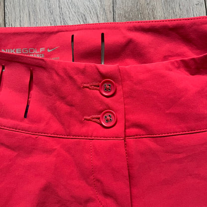 Nike Golf Tour Performance Golf Skirt is a women’s golf skirt in dark pink with belt loops integrated into the waistband. The side and lower hem outlines are finished in purple, and the skirt features front and back pockets with a button closure. An embroidered Nike logo is placed at the front