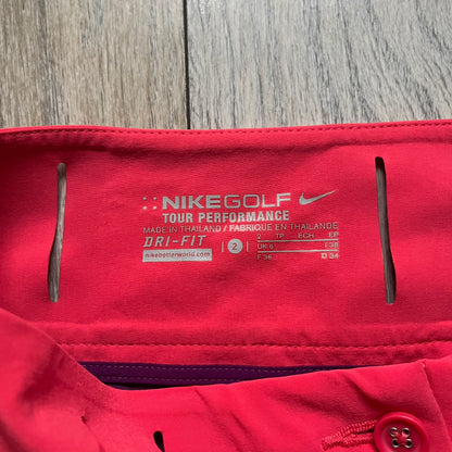 Nike Golf Tour Performance Golf Skirt is a women’s golf skirt in dark pink with belt loops integrated into the waistband. The side and lower hem outlines are finished in purple, and the skirt features front and back pockets with a button closure. An embroidered Nike logo is placed at the front
