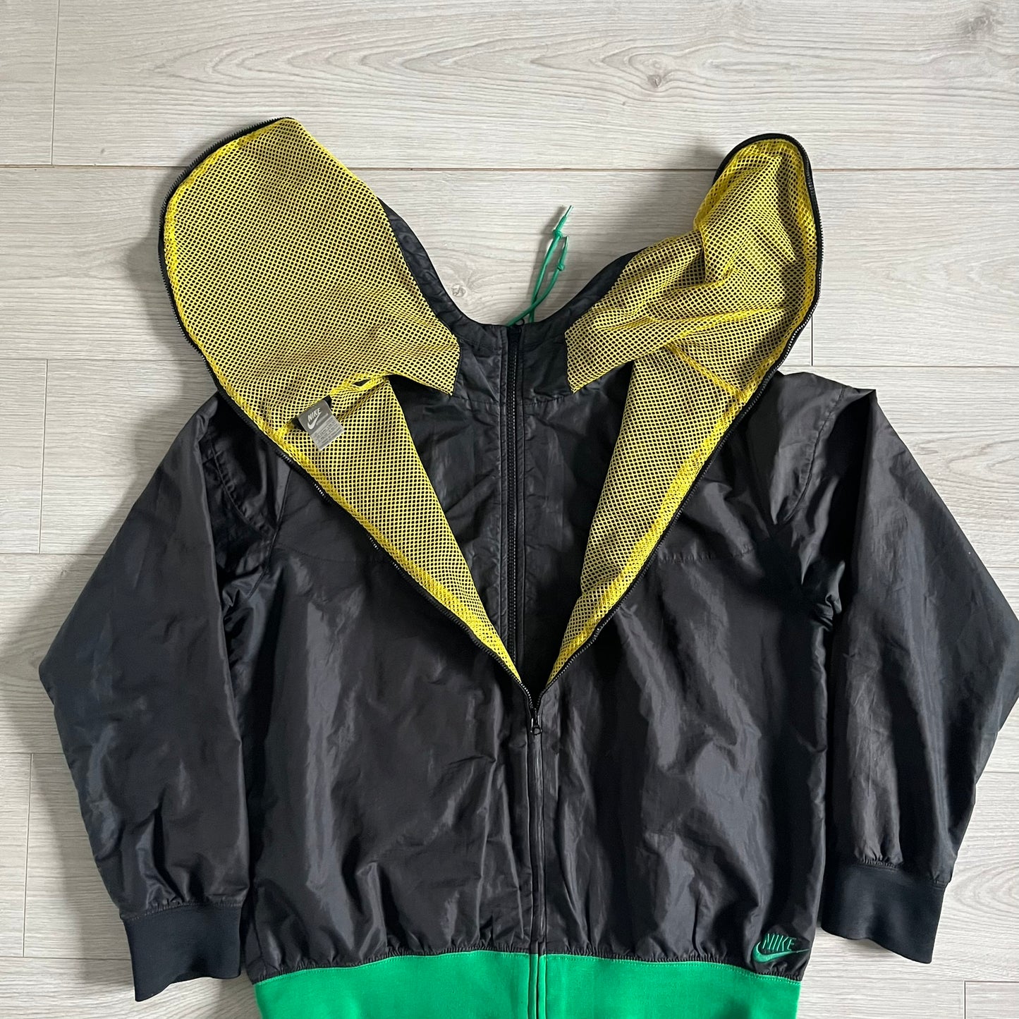 Nike Jamaica Olympics 2008 Split Windbreaker designed by Jarrett Reynolds. Features a black base with a yellow cross on the front inspired by the Jamaican flag. Green bottom hem and details. Dual side zippers allow the jacket to split in half and be combined with other pieces from the collection, with a small Jamaica flag detail inside the pocket.