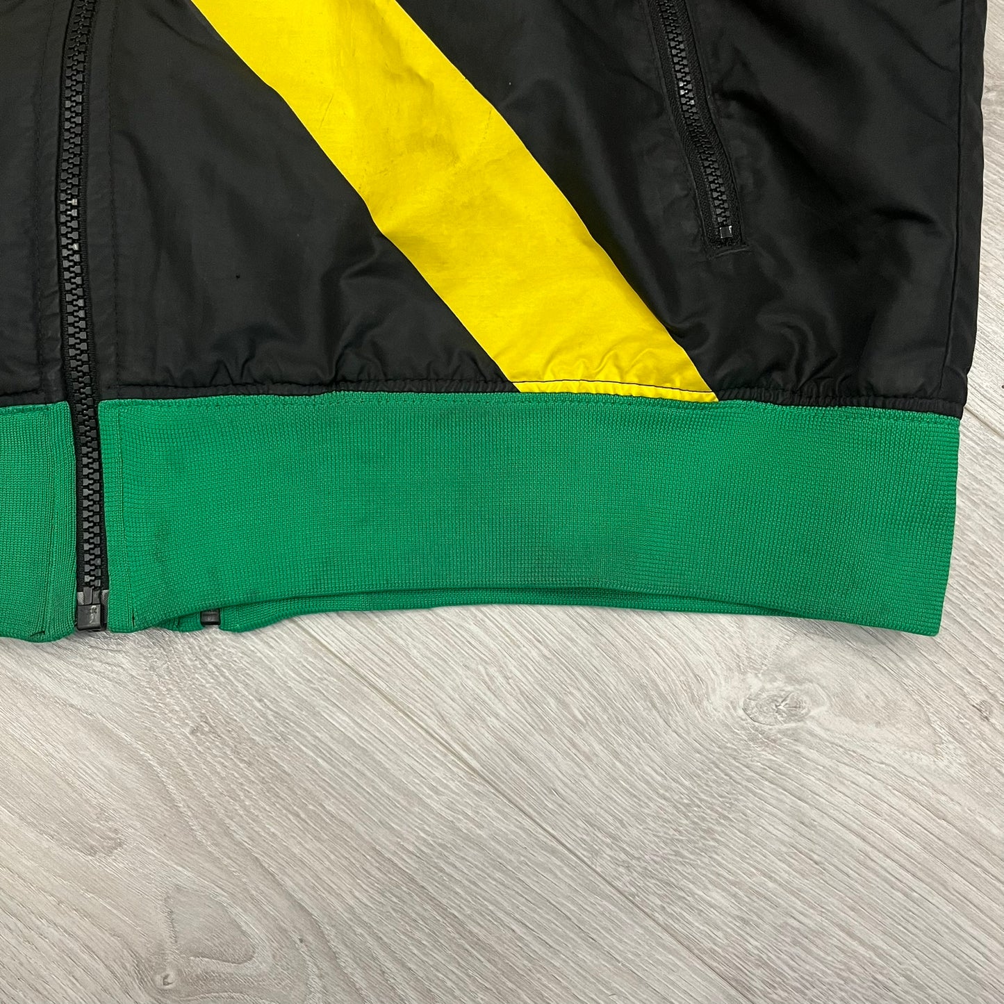 Nike Jamaica Olympics 2008 Split Windbreaker designed by Jarrett Reynolds. Features a black base with a yellow cross on the front inspired by the Jamaican flag. Green bottom hem and details. Dual side zippers allow the jacket to split in half and be combined with other pieces from the collection, with a small Jamaica flags detail inside the pocket.