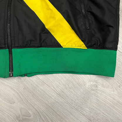 Nike Jamaica Olympics 2008 Split Windbreaker designed by Jarrett Reynolds. Features a black base with a yellow cross on the front inspired by the Jamaican flag. Green bottom hem and details. Dual side zippers allow the jacket to split in half and be combined with other pieces from the collection, with a small Jamaica flags detail inside the pocket.