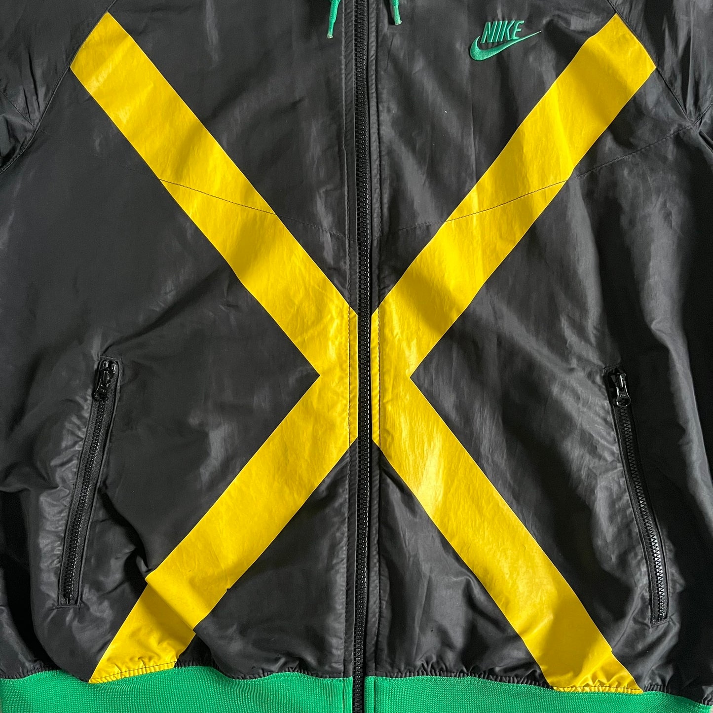 Nike Jamaica Olympics 2008 Split Windbreaker designed by Jarrett Reynolds. Features a black base with a yellow cross on the front inspired by the Jamaican flag. Green bottom hem and details. Dual side zippers allow the jacket to split in half and be combined with other pieces from the collection, with a small Jamaica flag detail inside the pocket.